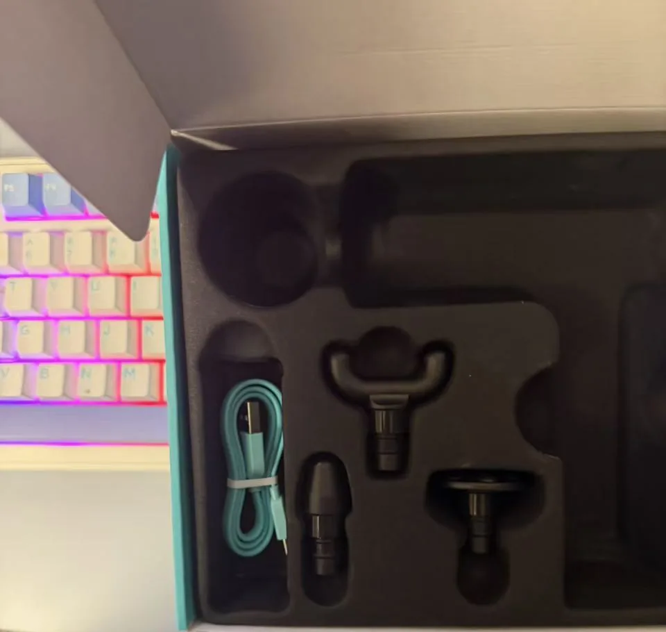 Open SKG F1 box showing the foam tray with a teal USB-C cable and interchangeable massage heads